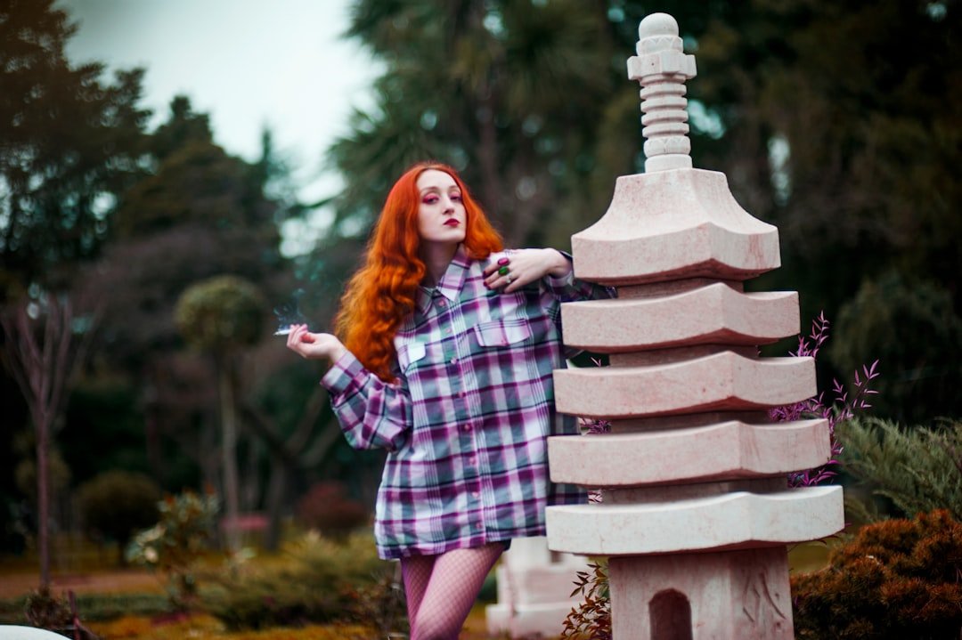 woman using cigarette while leaning on statue