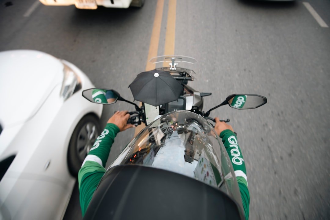a man riding a motorcycle down a street next to a white car